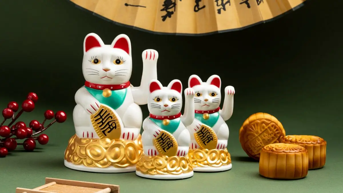 Trois figurines de Maneki Neko tenant une pièce, avec de la décoration